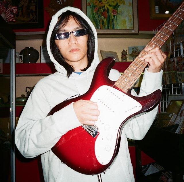 The musician Eyedress holds a red electric guitar.