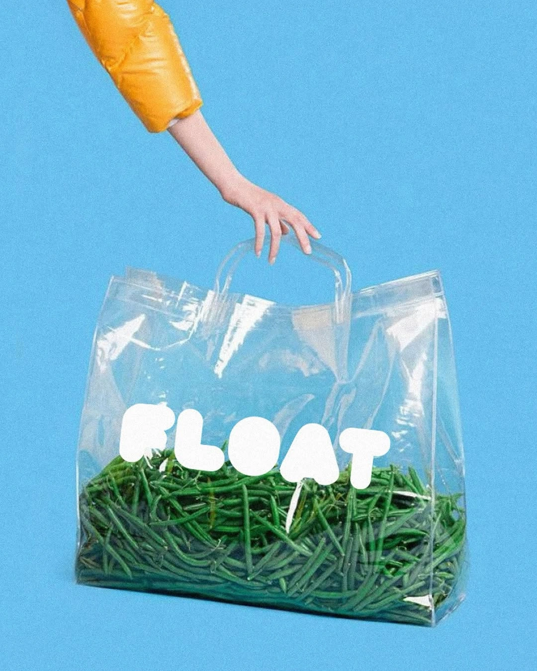 A still life product photograph featuring a transparent PVC tote bag filled with bright green shredded paper and white bubble-letter typography reading "FLOAT".
