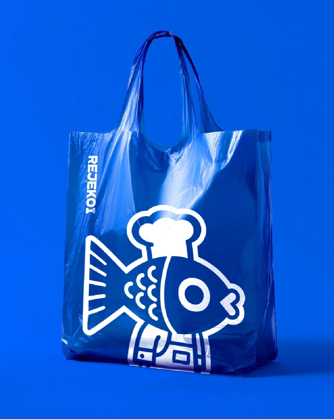 A bright blue plastic tote bag with a white line-drawn illustration of a fish wearing a chef's hat, shot against a solid blue background.