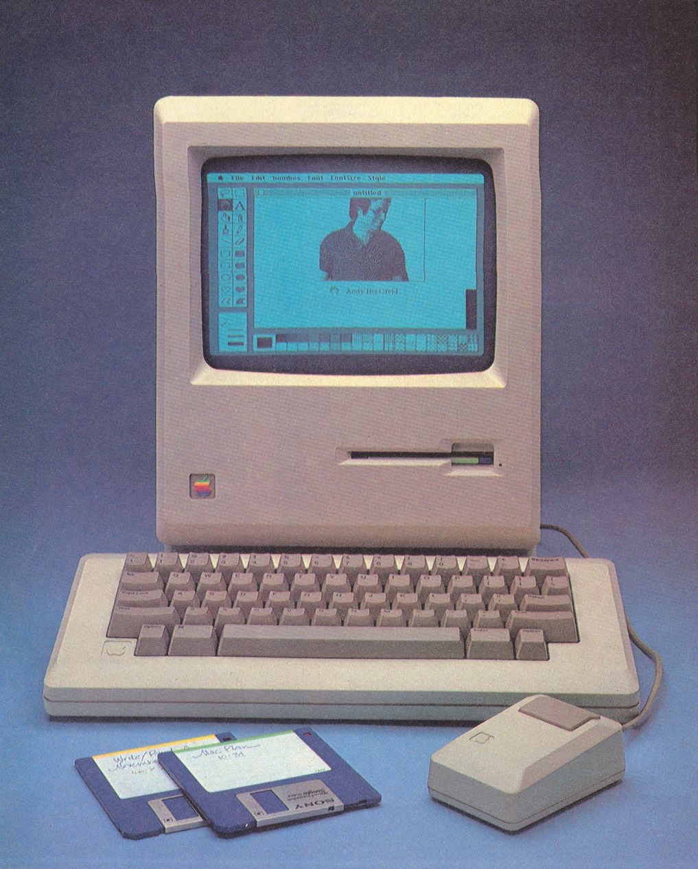 The original Apple Macintosh computer. The screen shows a self-portrait by Andy Hertzfeld in MacPaint.