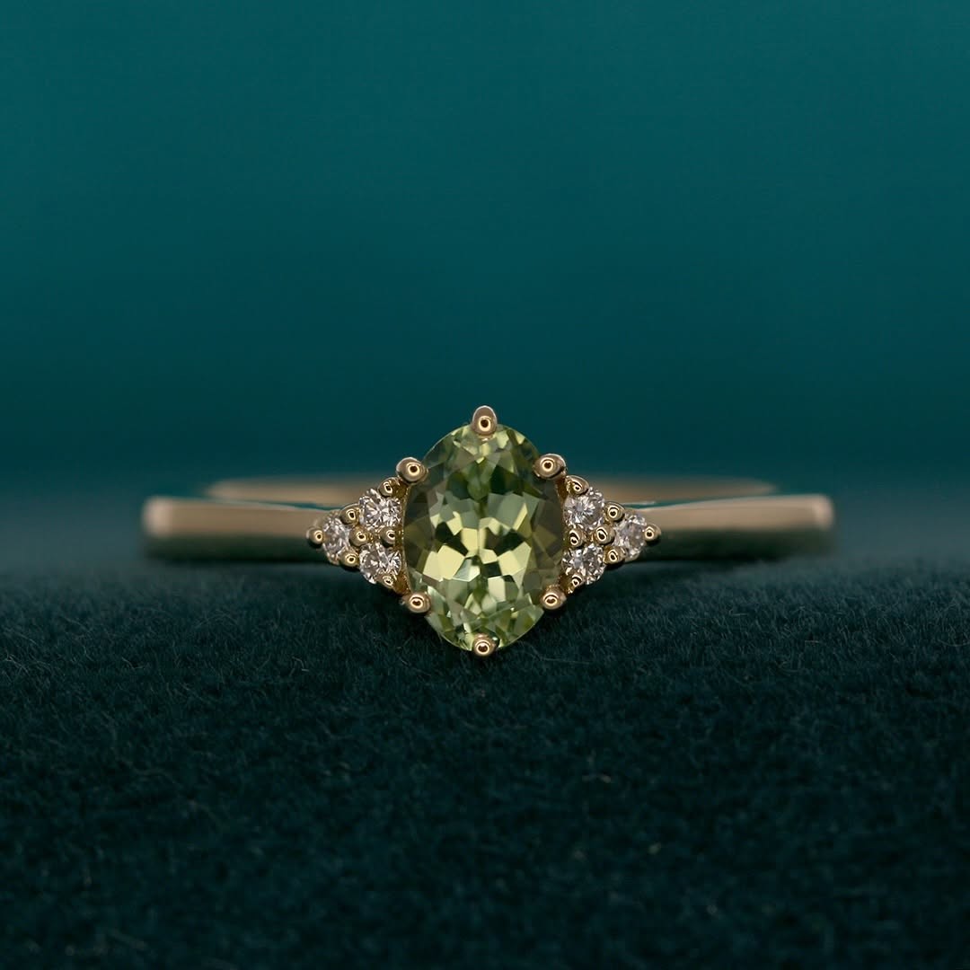 Gold engagement ring by Saint Teneu with a green tourmaline and diamond clusters.
