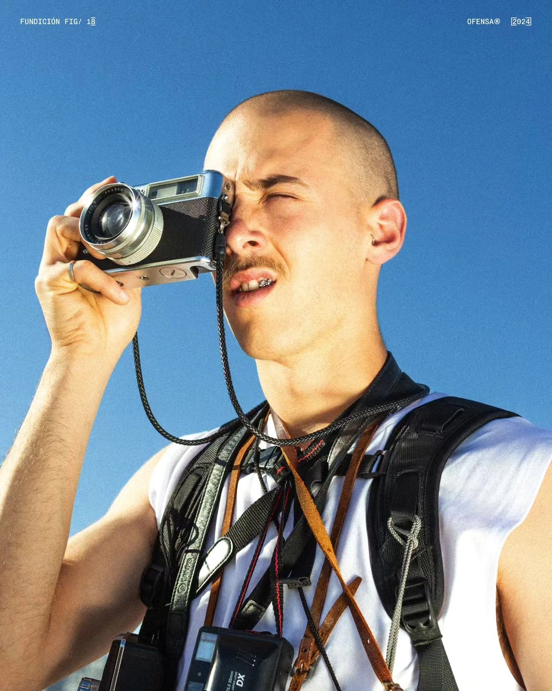 Portrait photograph of a man holding a vintage rangefinder camera against a clear blue sky.