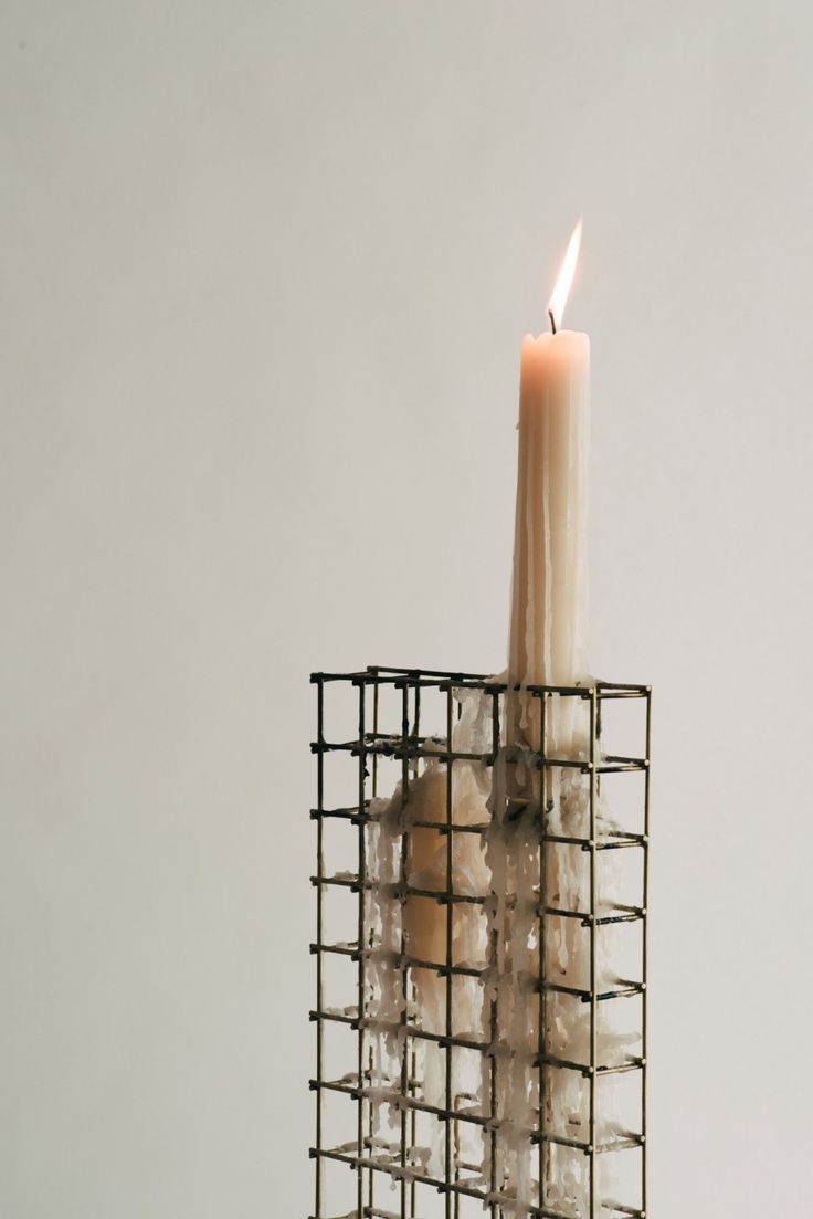 A lit candle melts over a gridded metal holder by TANZ.